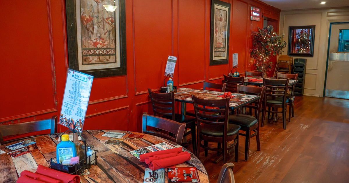 Restaurant interior with red walls, wooden tables with red napkins, and framed artwork