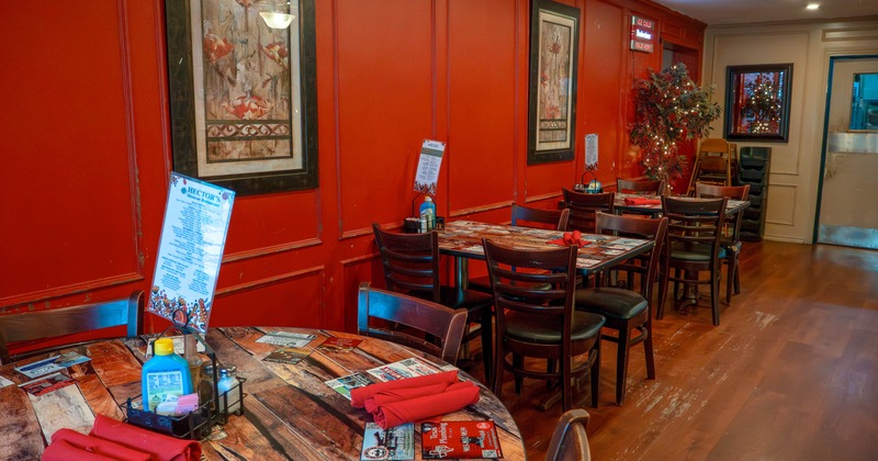 Restaurant interior with red walls, wooden tables with red napkins, and framed artwork