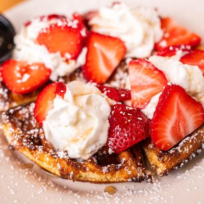 Waffles, with strawberries, whipped cream, and powdered sugar.
