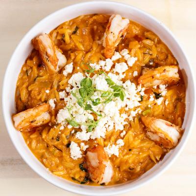 Bowl of creamy orange pasta with grilled shrimp and crumbled cheese.