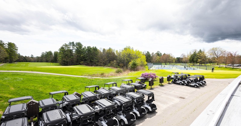 Golf course with golf carts parked, tennis courts in the background, and lush green fairways