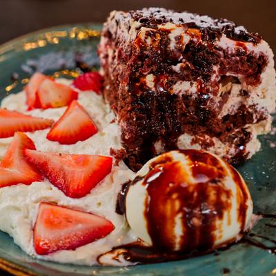 A slice of black forest cake with ice cream, whipped cream, and sliced strawberries.