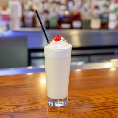 Pina Colada served in a tall glass on a wooden bar counter, garnished with a cherry.