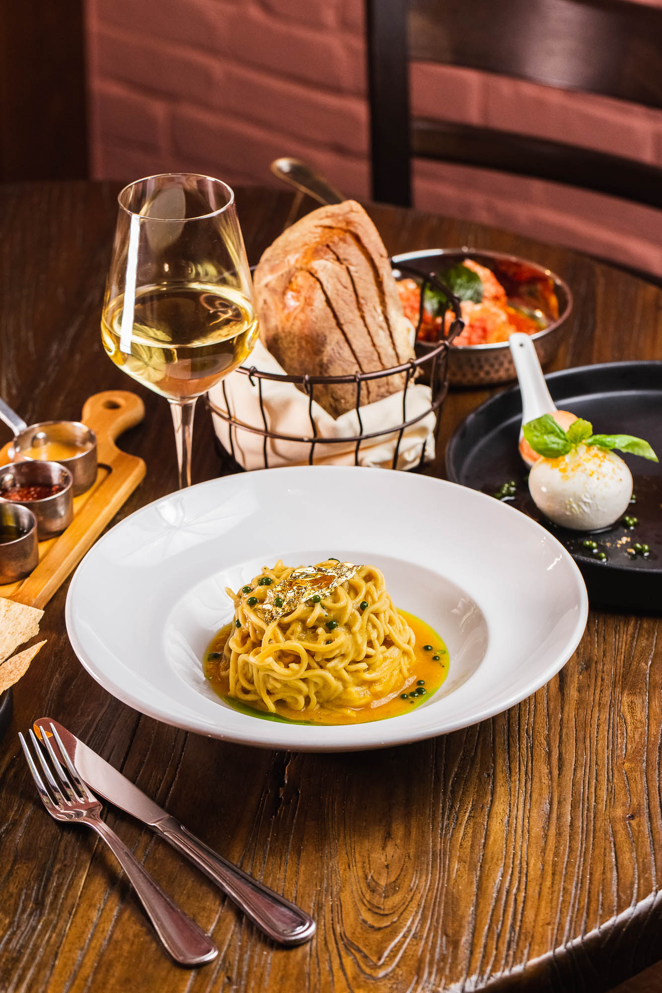 Spaghetti in golden tomato sauce on a table with white wine glass, bread and condiments