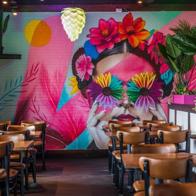 Interior with tables, chairs and large colourfull mural on the wall.