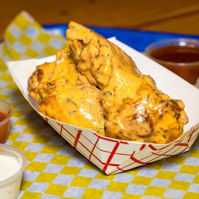 Buffalo chicken wings coated in creamy orange sauce served in a paper tray.