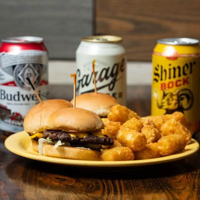Plate of sliders with tater totos, served on the table with three cans of beer.