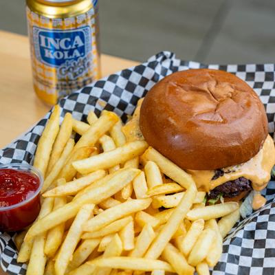 Burger with fries on checkered paper beside an opened can of Inca Kola.