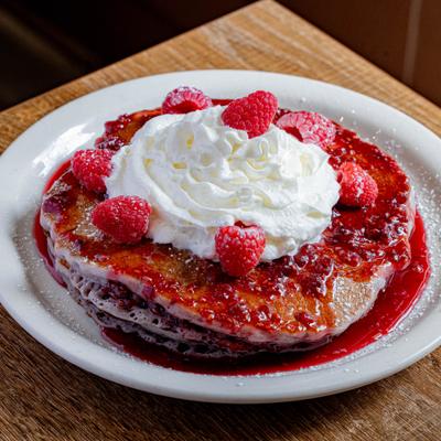 Raspberry Pancakes topped with whipped cream and fresh berries.