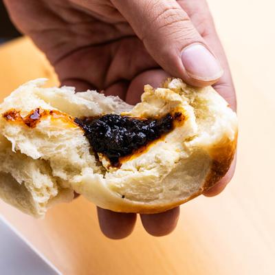 A hand holding a torn bun filled with dark jam.