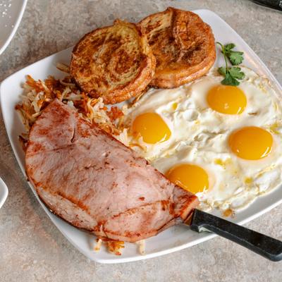 Breakfast platter featuring fried eggs, grilled ham, French toast and hash browns.