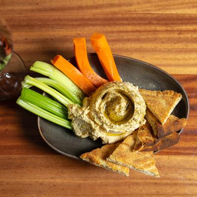 Plate of hummus with celery, carrot sticks and pita bread on a wooden table, top view