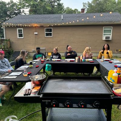 People sitting at an outdoor table behind a grill.