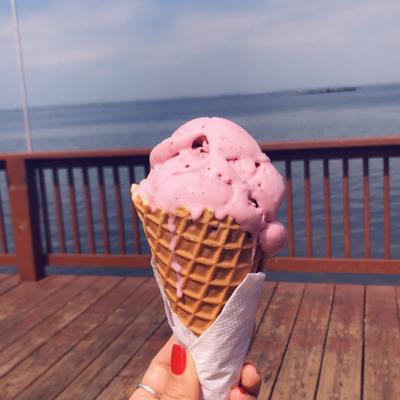 Person holding strawberry ice cream cone with sea view.