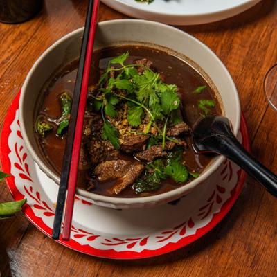 Thai Boat Noodle Soup with beef and fresh herbs, served with chopsticks and a spoon.