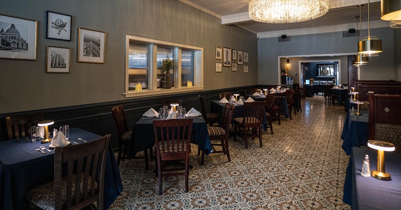 Elegant restaurant interior with tables set beside a gray-painted wall, adorned with framed artwork