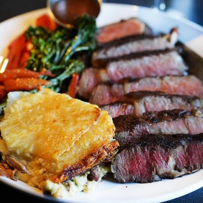 Sliced steak with cheesy potato gratin, broccolini, and roasted carrots.