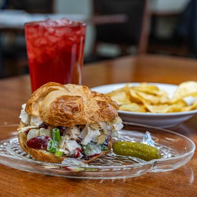 A croissant sandwich with chicken salad served with an iced red drink and chips.