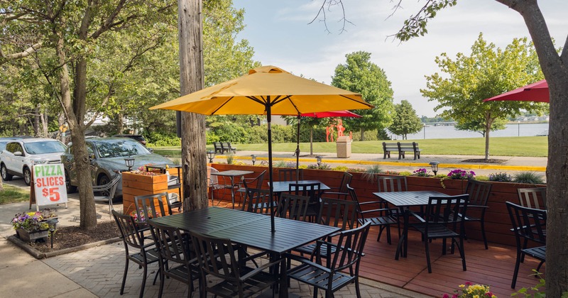 Outdoor patio with tables, chairs, and a yellow umbrella, surrounded by trees and flowers