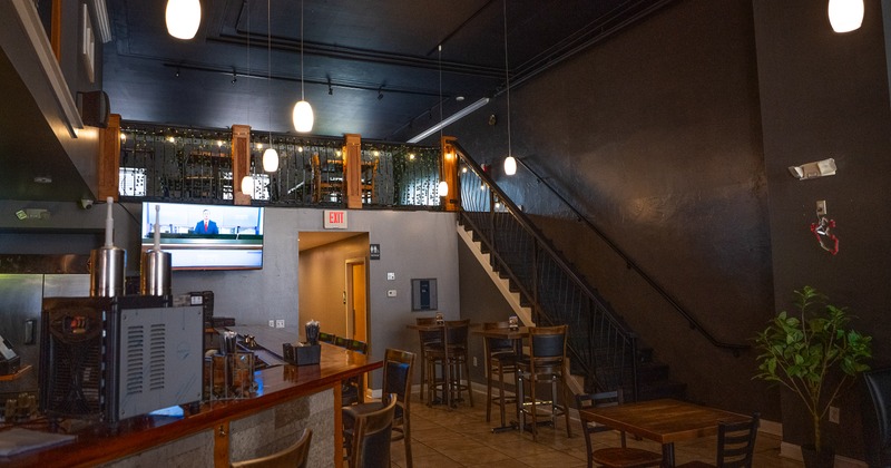 Modern restaurant interior with tables and chairs, and a staircase leading to an upper dining area