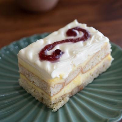 Tiramisu with white frosting and a fruit swirl sits on sits on a green, scallop-edged plate.