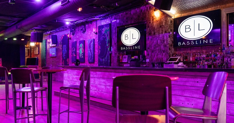 An interior view of a bar with purple lighting, wooden furniture, a long bar counter