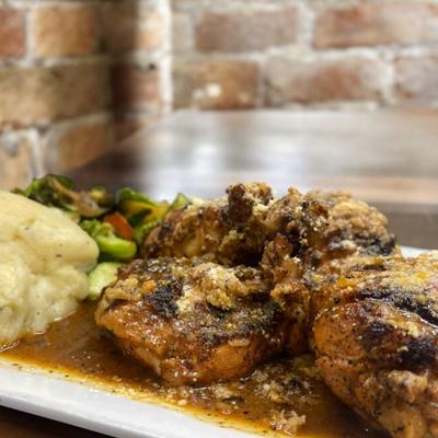 A plate of seasoned grilled chicken with mashed potatoes and sauteed vegetables.