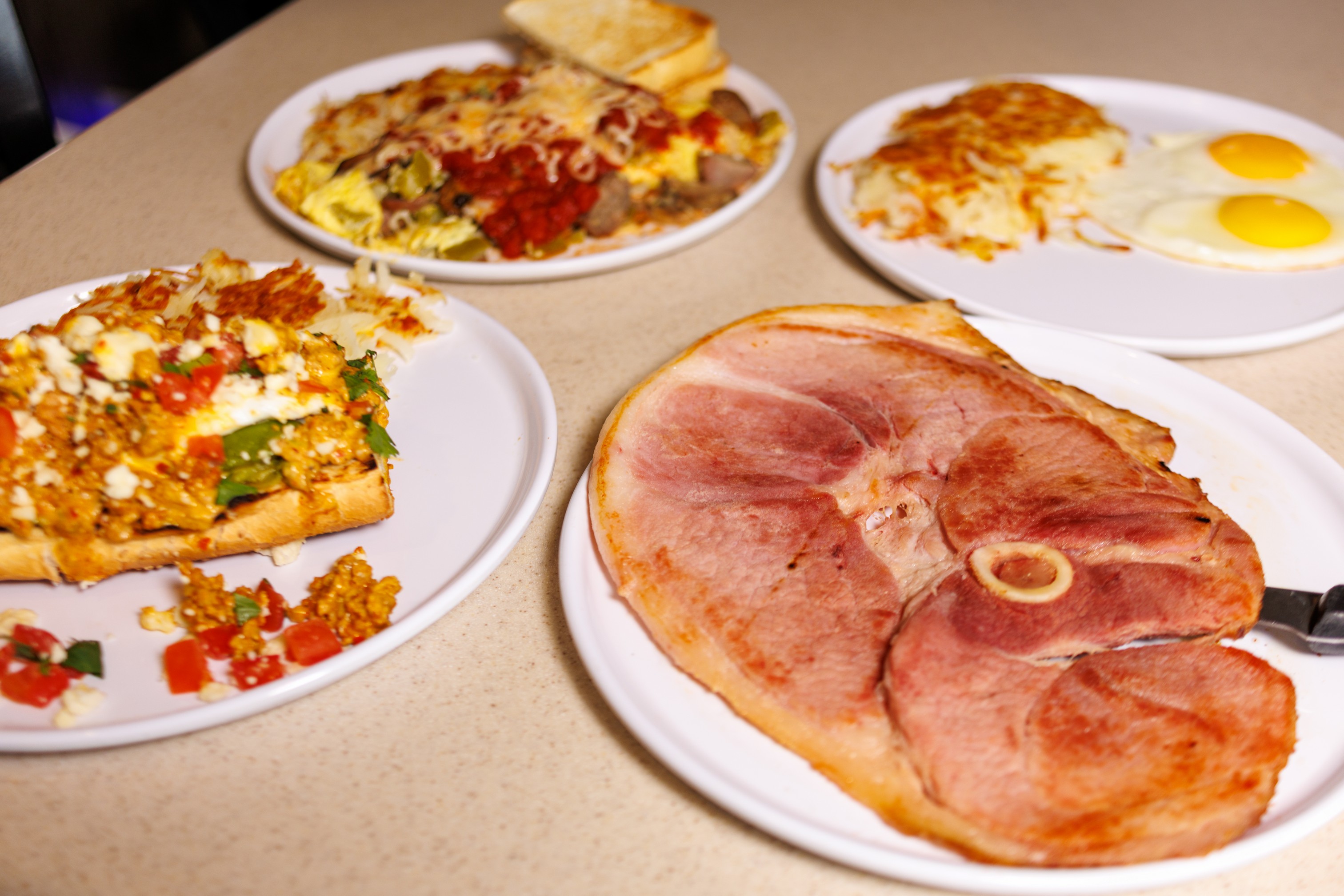 A large ham steak served alongside breakfast platters of eggs and scrambles