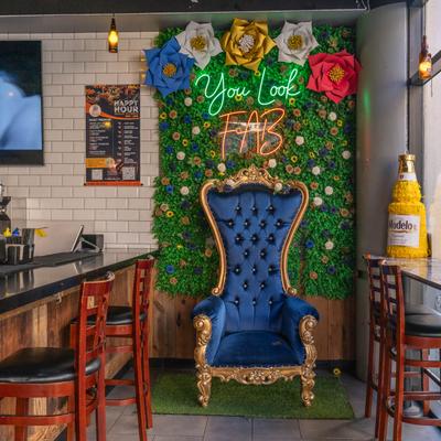 Interior featuring a blue throne chair against a green flower wall with colorful neon lights.