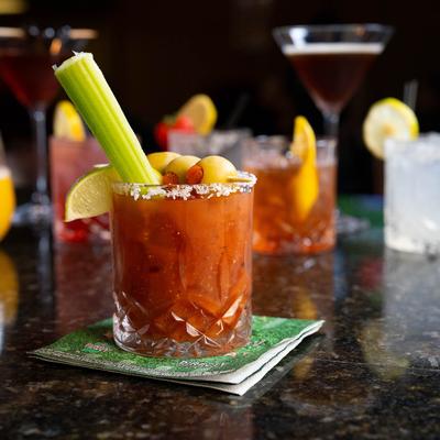 Bloody Mary placed on a bar counter with assorted cocktails in the background.
