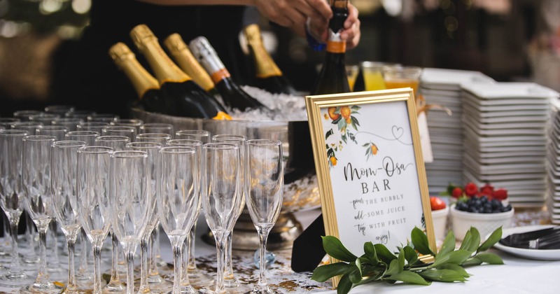 Rows of empty champagne glasses and buckets with champagne on a table with fruit and tableware