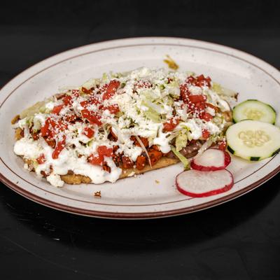 Huarache topped with diced tomatoes, lettuce, sour cream, and queso fresco.