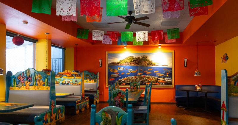 Interior of a brightly colored restaurant with papel picado banners and marine-themed decor