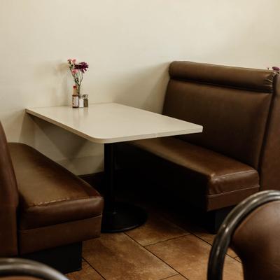 Restaurant booth with brown leather seating and a white table with flowers and condiments.