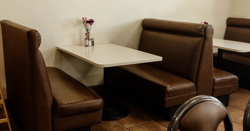 Restaurant booth with brown leather seating and a white table with flowers and condiments
