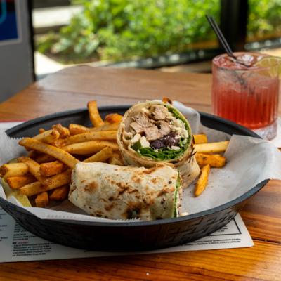 Grilled chicken wrap served with seasoned french fries and a refreshing red cocktail.