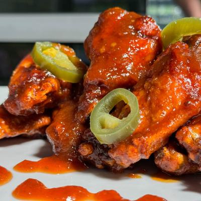 Wings covered in sauce with sliced pickled jalapenos.