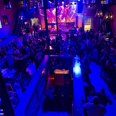 Overhead view of a crowded dance floor and stage bathed in blue and purple party lights.