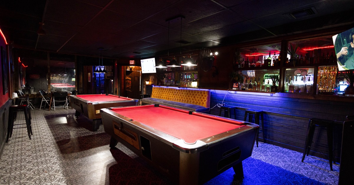 Interior with two red felt pool tables, patterned tile flooring, bar stools, bar