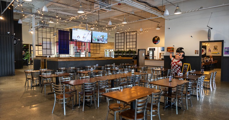 Modern restaurant interior with wooden tables, sports screens, and a large mascot