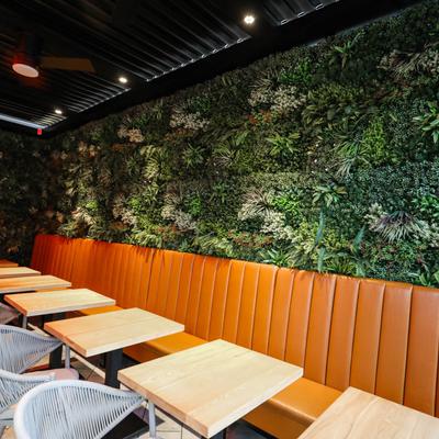 Banquette seating, tables and chairs by a wall decorated with faux greenery