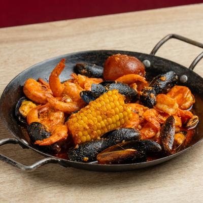 Pan of seafood boil with shrimp, mussels, clams, corn cob and potato.