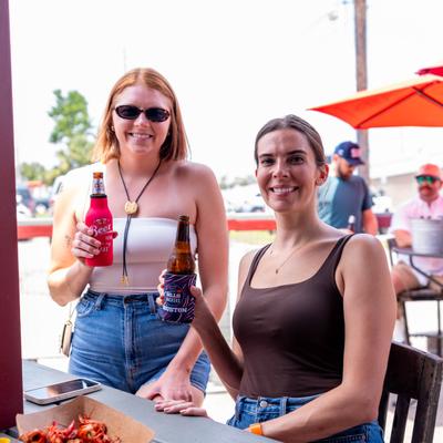 Two friends posing together with beer bottles at a patio table.