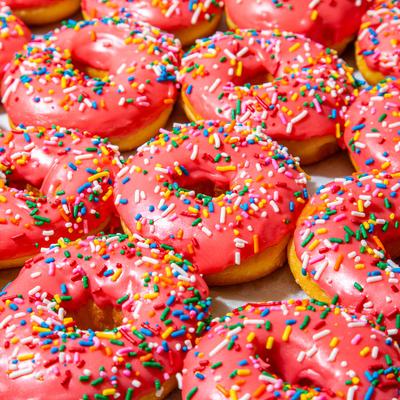 A close-up of numerous pink-frosted doughnuts covered in colorful sprinkles.