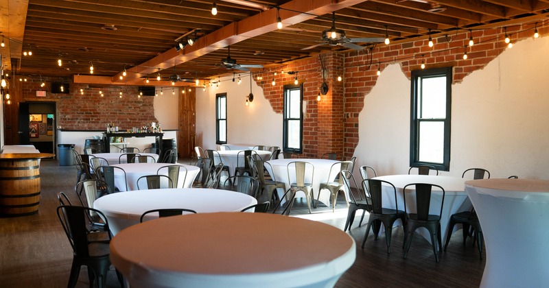 Interior dining area with round tables with white tablecloths, and metal chairs