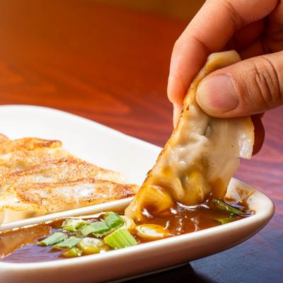 Pan fried dumpling dipped into soy sauce garnished with chopped scallions.