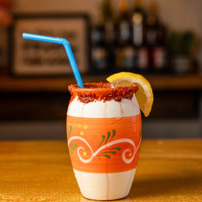 Cocktail served in a handcrafted clay cup with a chili rim and lemon slice garnish.