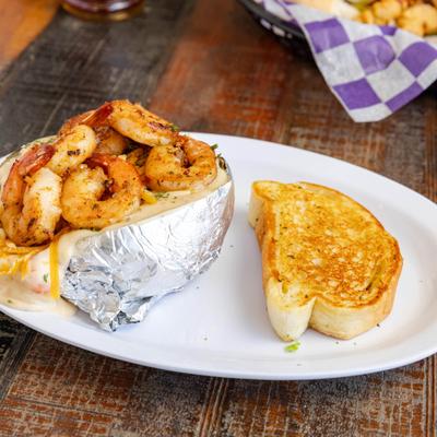 Loaded baked potato topped with shrimp alongside a slice of toasted bread.