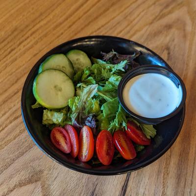 Garden salad featuring mixed greens, cucumbers, cherry tomatoes and a cup of dressing.
