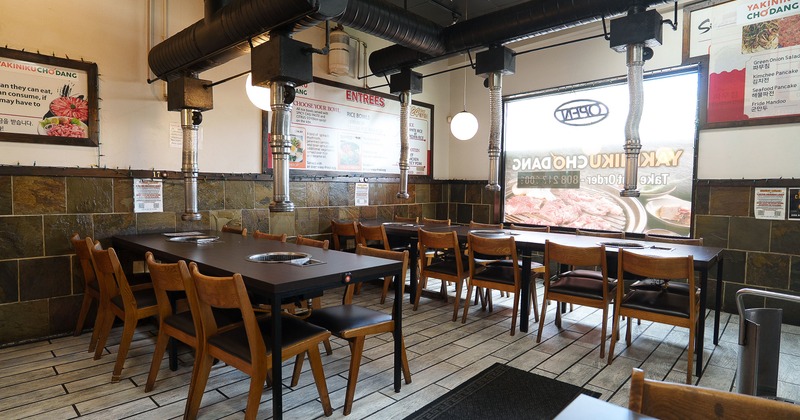 Korean BBQ restaurant with tables with built-in grills and ventilation pipes above each seating area